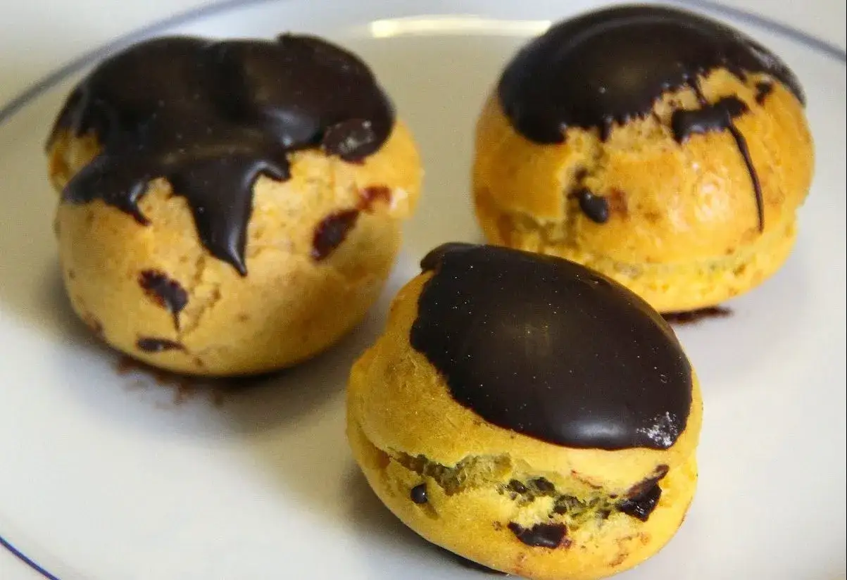 Tre deliziose teste di turco, bign&egrave; ripieni e ricoperti di cioccolato fondente, pronti per essere gustati.
