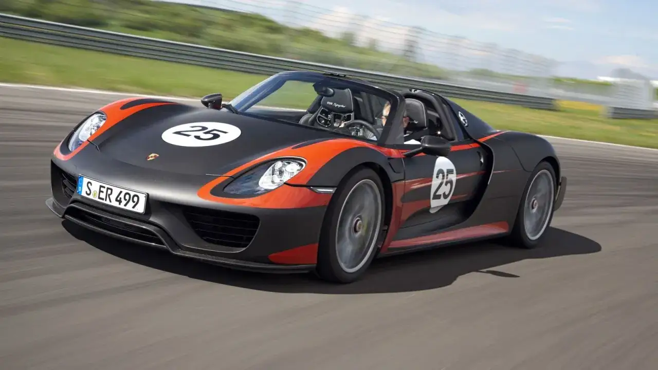 Czarny Porsche 918 Spyder z pomarańczowymi akcentami i numerem 25 pędzi po torze wyścigowym.