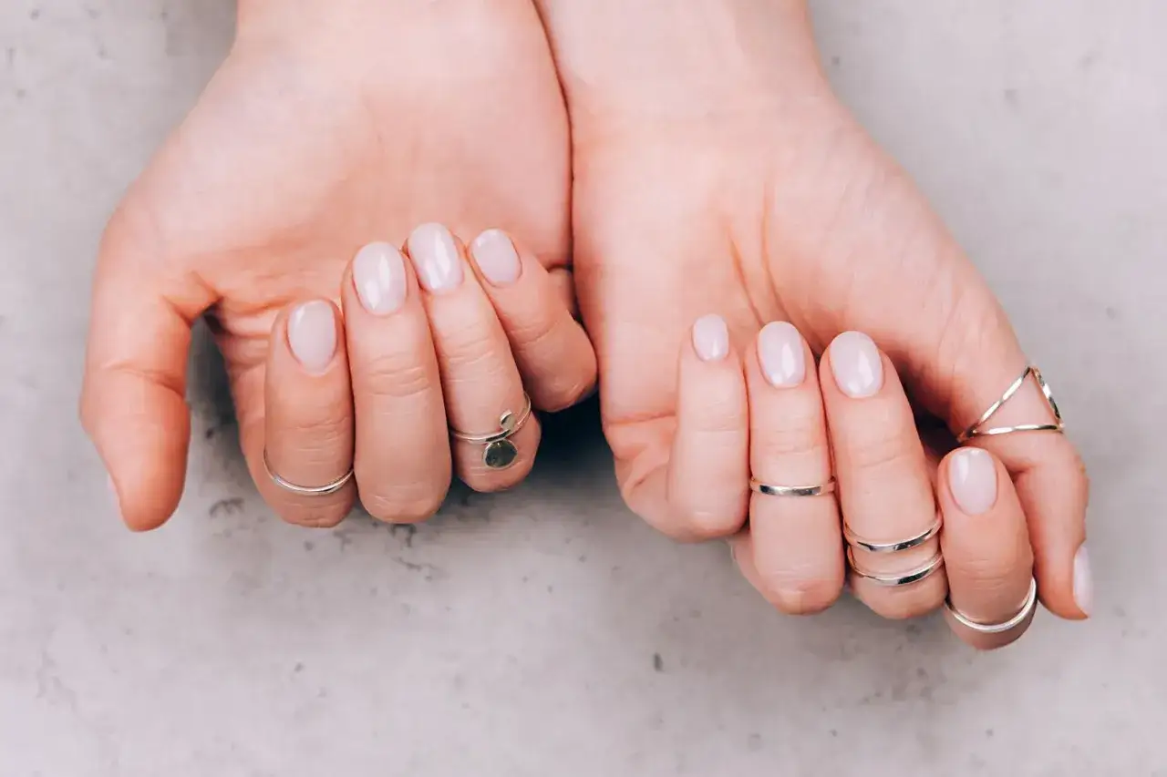 Delikatne, różowe paznokcie clean girl z subtelnymi srebrnymi pierścionkami. Idealny manicure na co dzień.