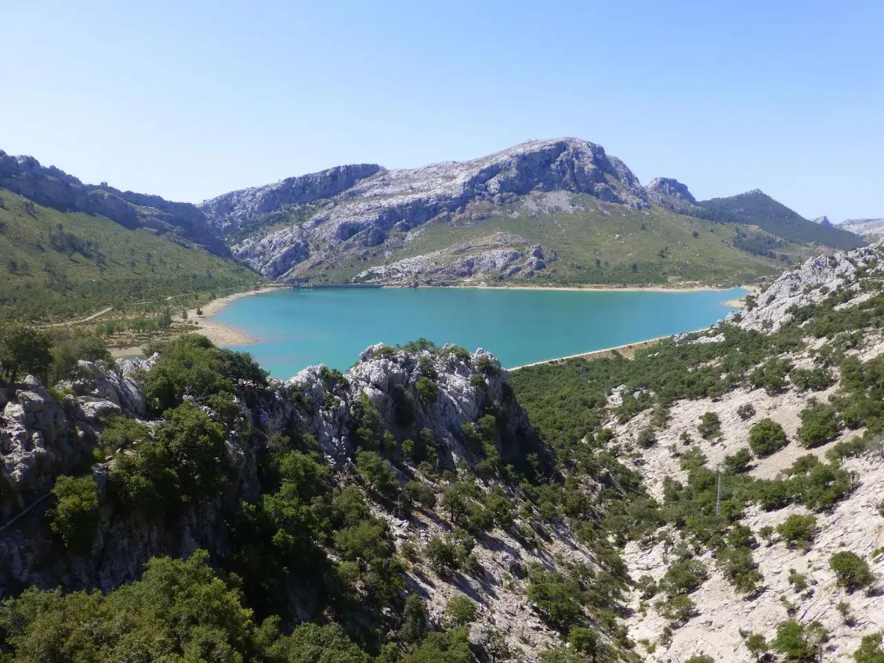 Impresionante vista de los lagos en Mallorca, rodeados de monta&ntilde;as rocosas y vegetaci&oacute;n verde bajo un cielo azul claro.