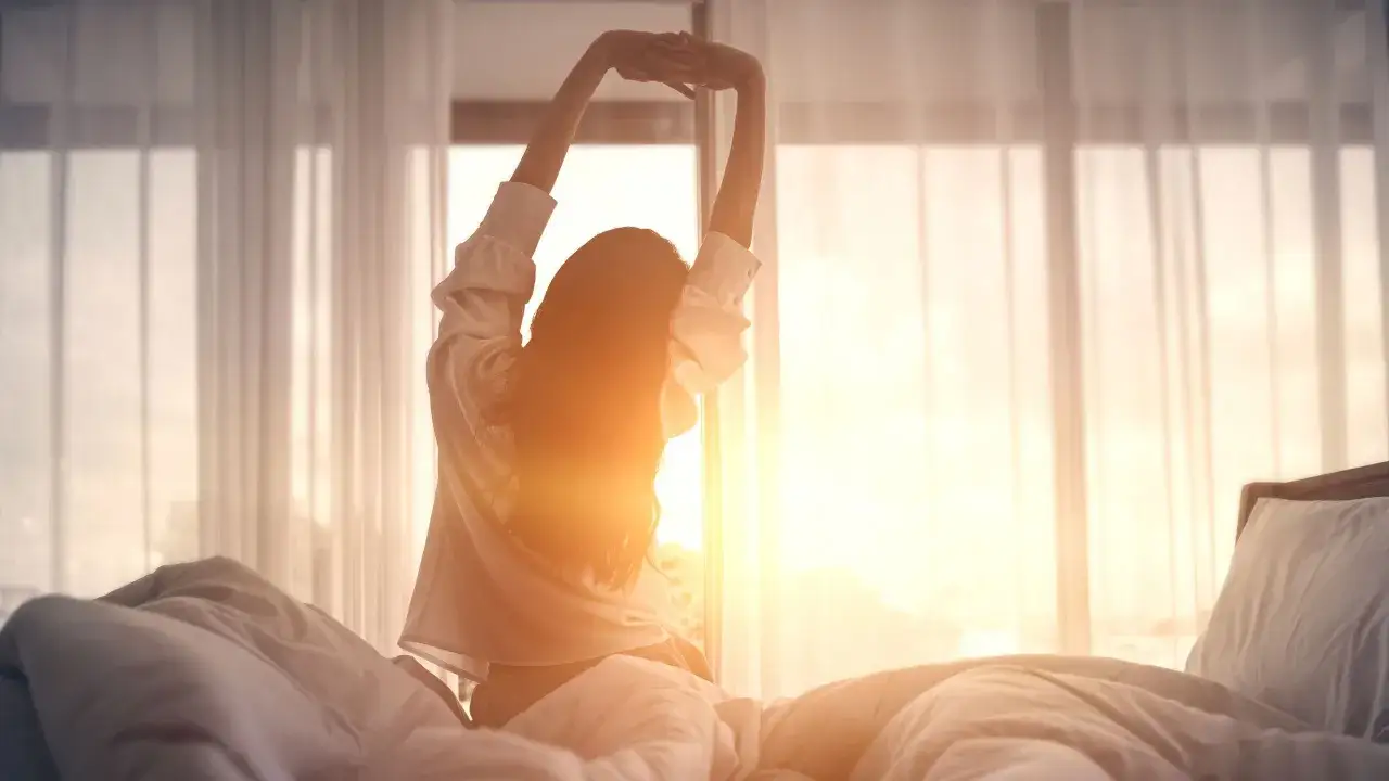 A woman stretches in bed as the sun rises, a perfect way to wake yourself up.