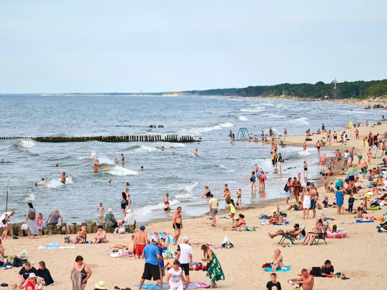 Tłum ludzi cieszy się słońcem i kąpielą na najszerszej plaży w Polsce. Fale Bałtyku łagodnie rozbijają się o brzeg.