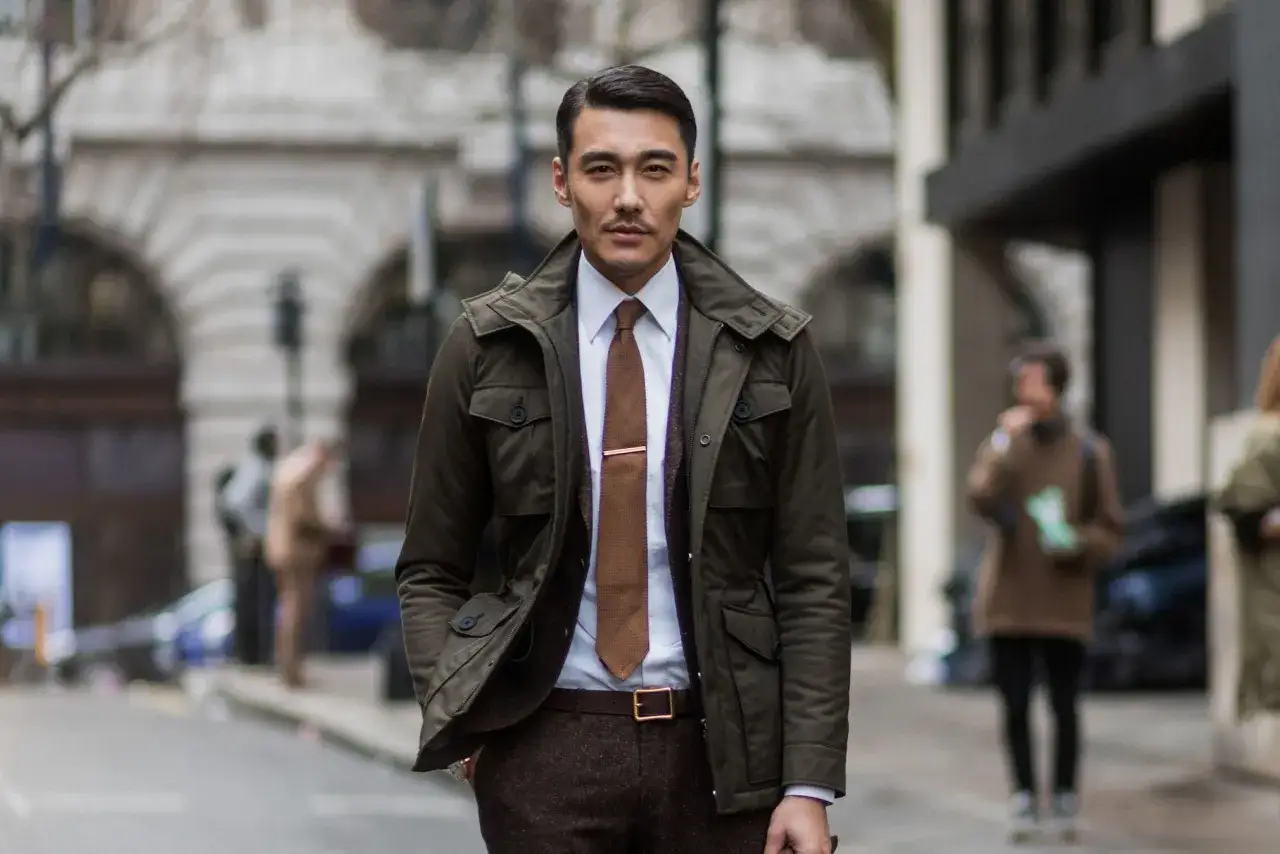 Hombre con vestimenta business casual: chaqueta verde, camisa blanca, corbata marrón y pantalón de tweed.