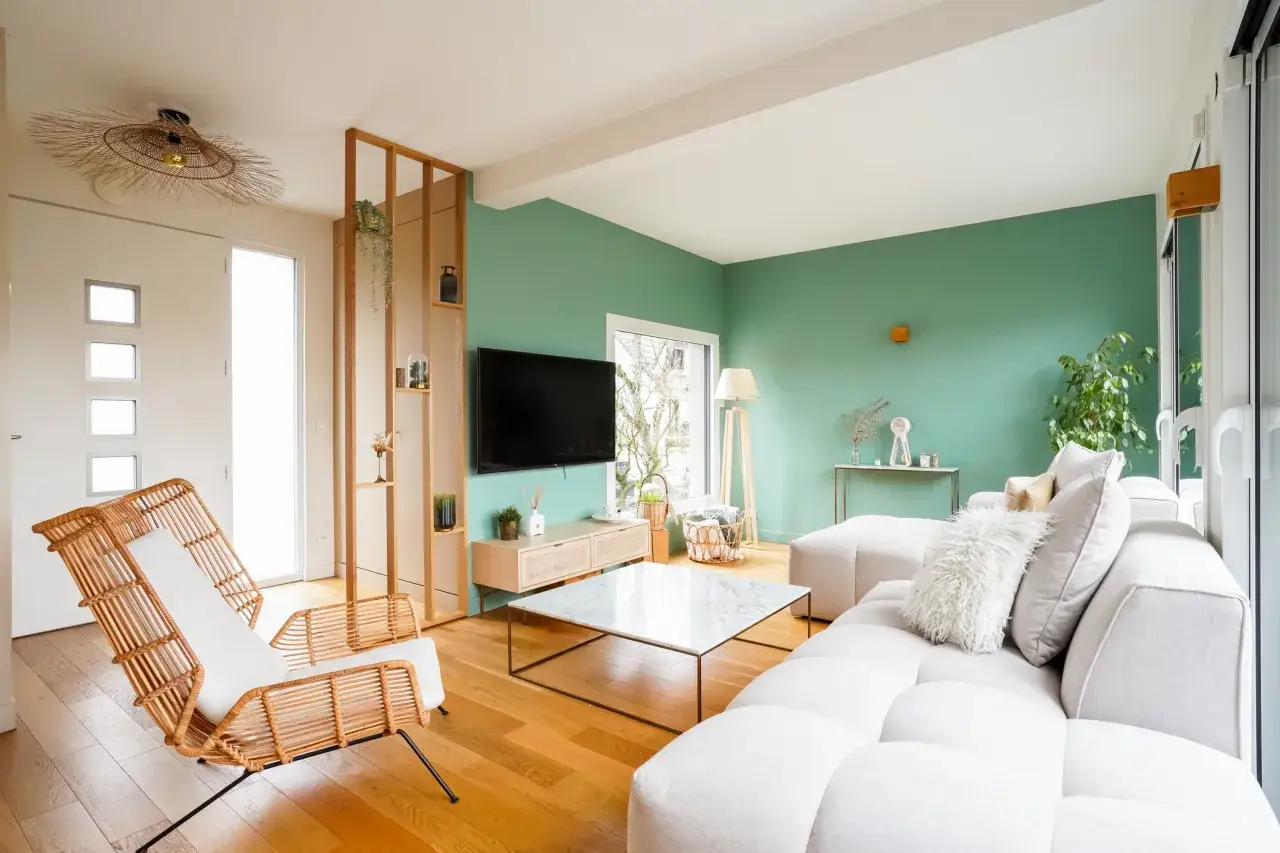 Salon lumineux aux murs d'un vert doux, avec un canapé blanc, des fauteuils en rotin et une table basse en marbre. Les nuances de vert apportent une touche de fraîcheur.