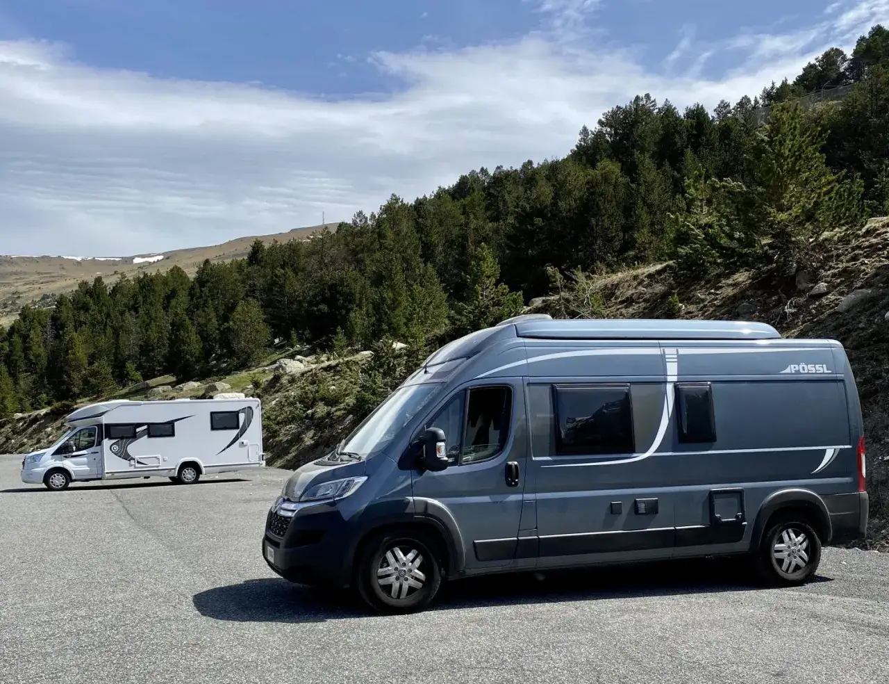 Deux camping-cars stationnés sur une aire de repos en Andorre, avec une forêt de pins en arrière-plan.