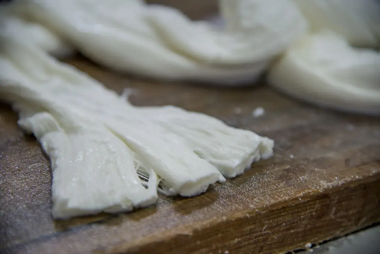 Formaggio pasta filata appena lavorato, con fili bianchi e morbidi su un tagliere di legno.