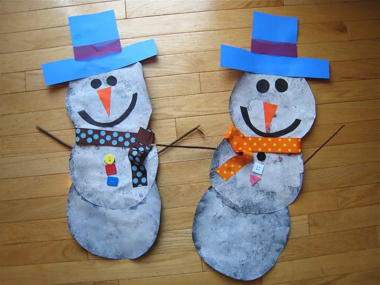 Zwei selbstgebastelte Schneemänner mit blauen Hüten und bunten Schals, bereit für den Winter. Perfekt zum Schneemann basteln!