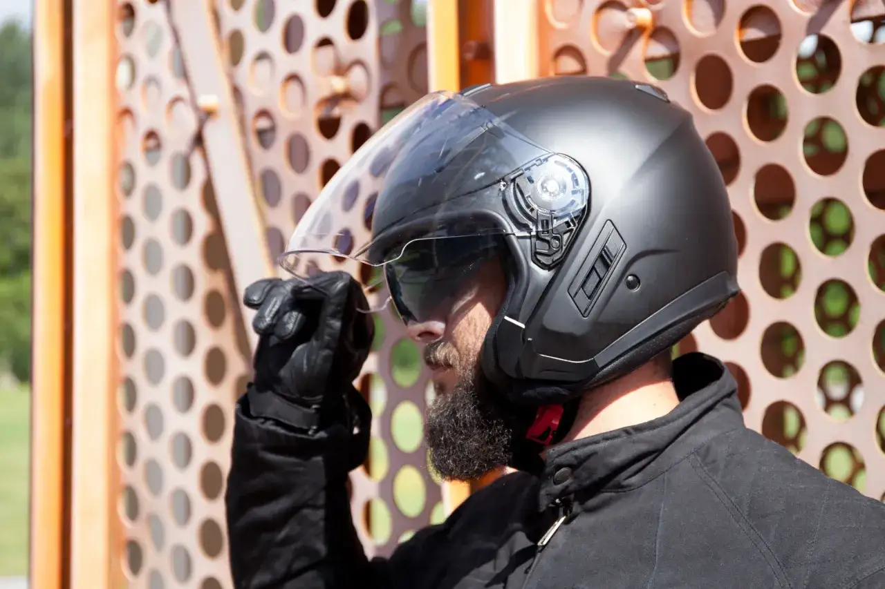 Motociclista con casco negro, ajustando la visera. El casco cuenta con las homologaciones cascos moto necesarias para circular con seguridad.