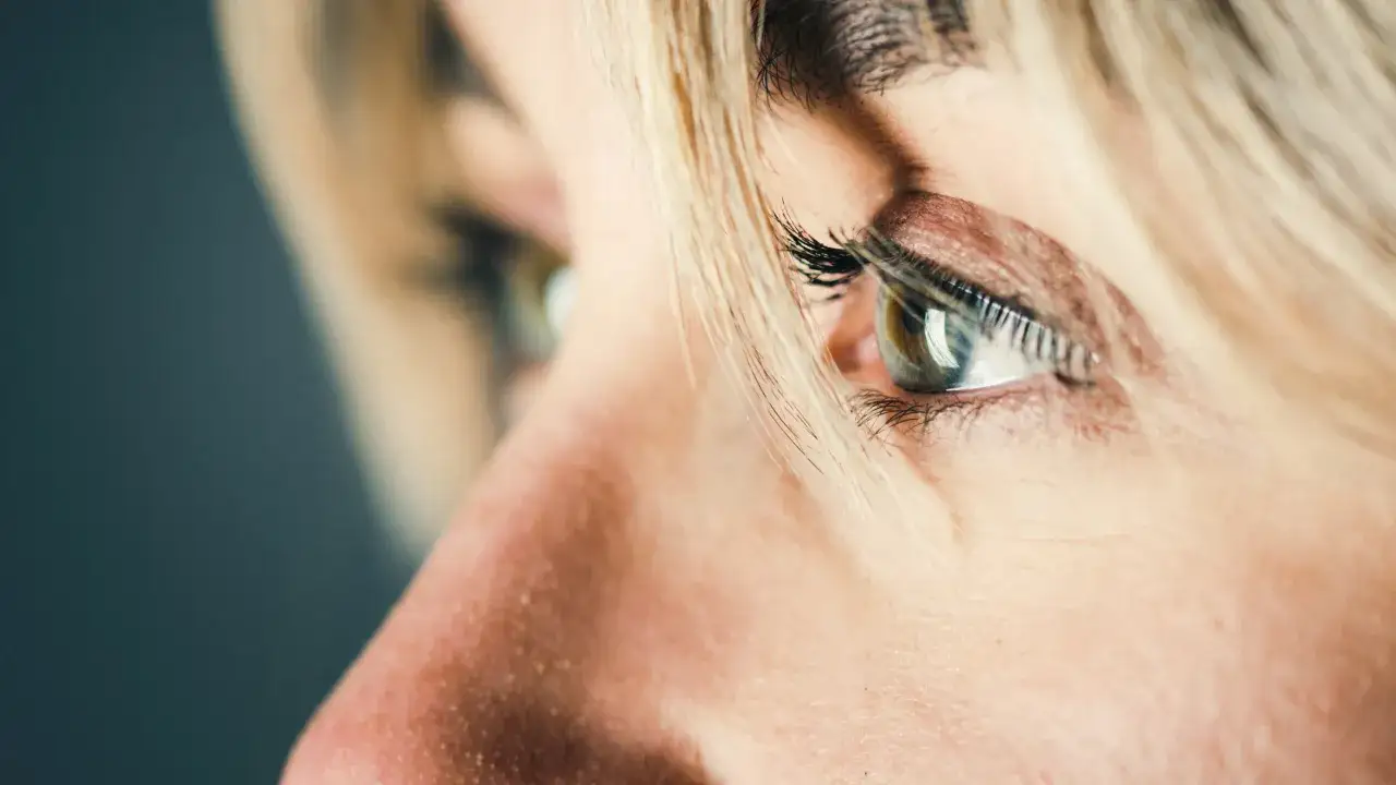 Zbliżenie na oko kobiety, z widocznym makijażem i blond włosami. Może symbolizować troskę o ciśnienie w oku.