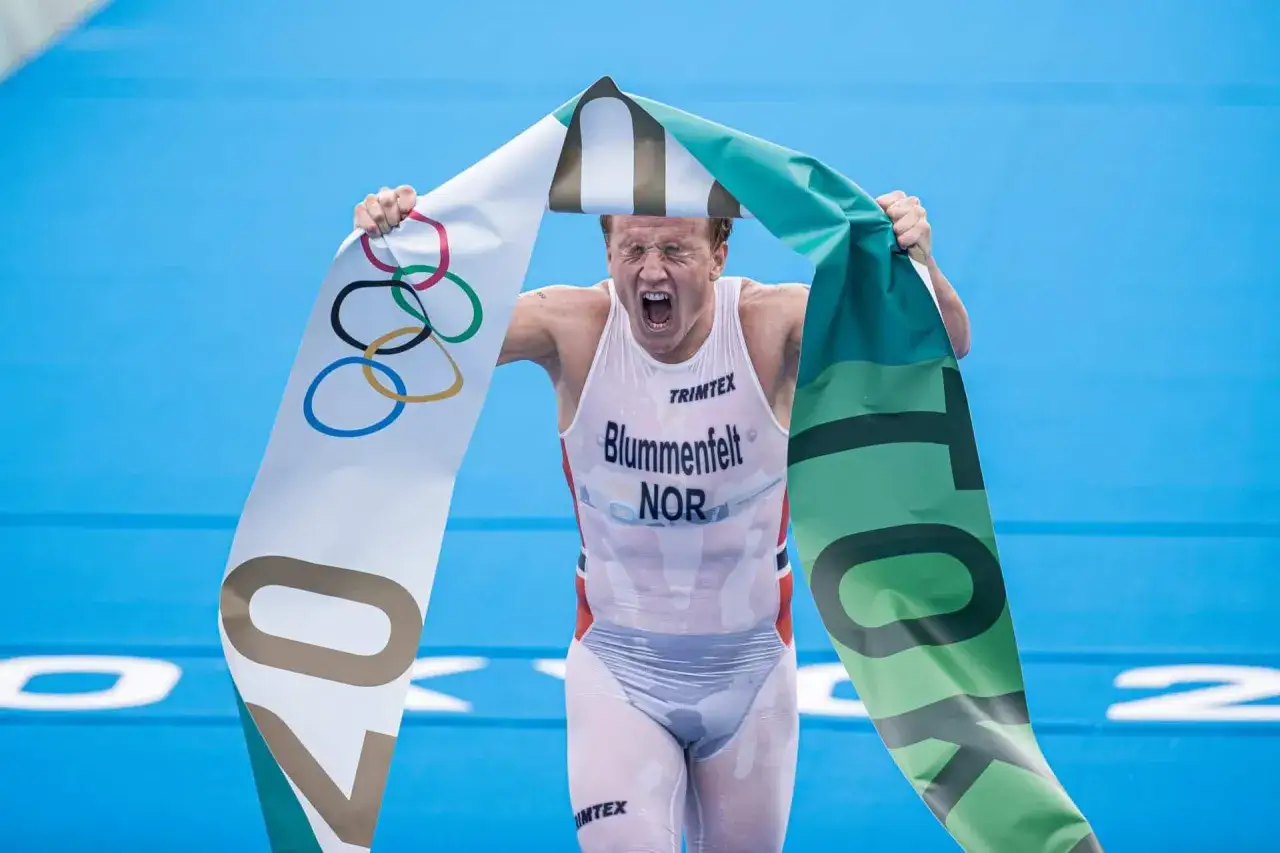 Kristian Blummenfelt feiert seinen Olympiasieg mit der norwegischen Flagge und dem olympischen Logo. Sein hoher vo2 max wert erm&ouml;glichte diese Leistung.