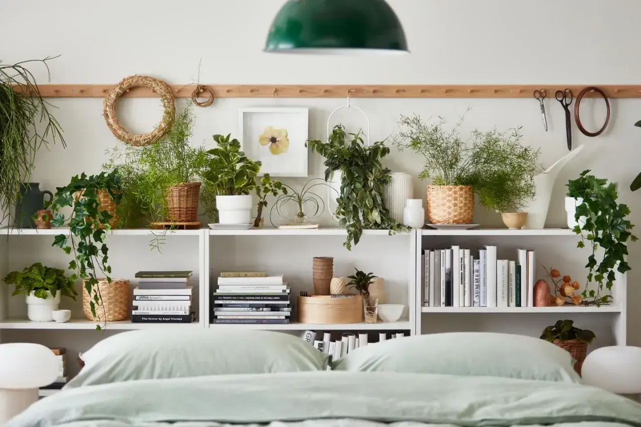 Grüne Pflanzen im Schlafzimmer schaffen eine beruhigende Atmosphäre. Auf weißen Regalen stehen diverse Topfpflanzen, Bücher und Dekoartikel.