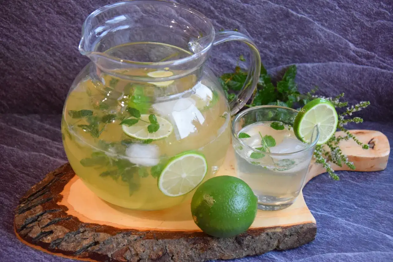 Dzbanek i szklanka orzeźwiającego napoju z limonką i miętą, idealnego do mojito. Obok leży świeża limonka.