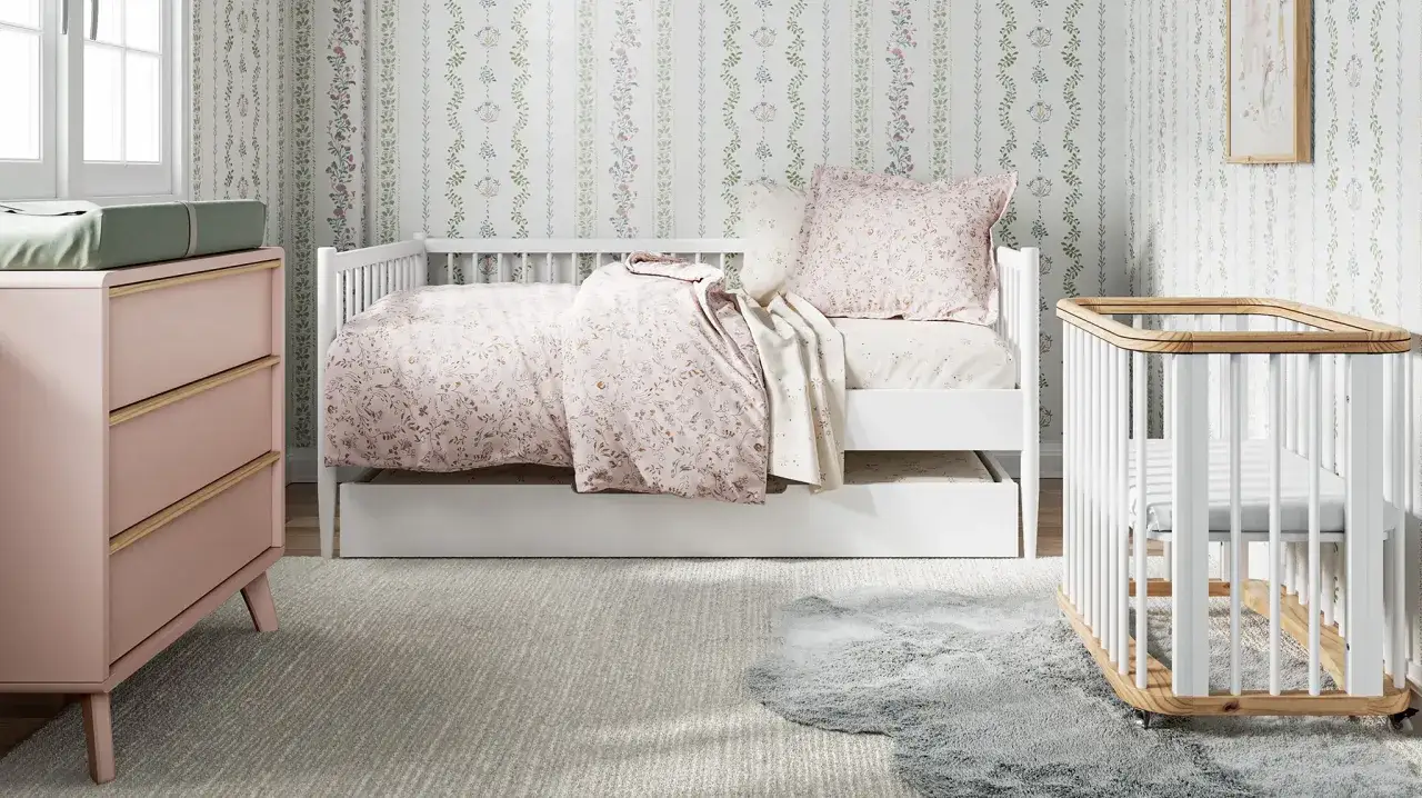 A charming small nursery features a white daybed with floral bedding, a pink dresser with a changing pad, and a white crib.