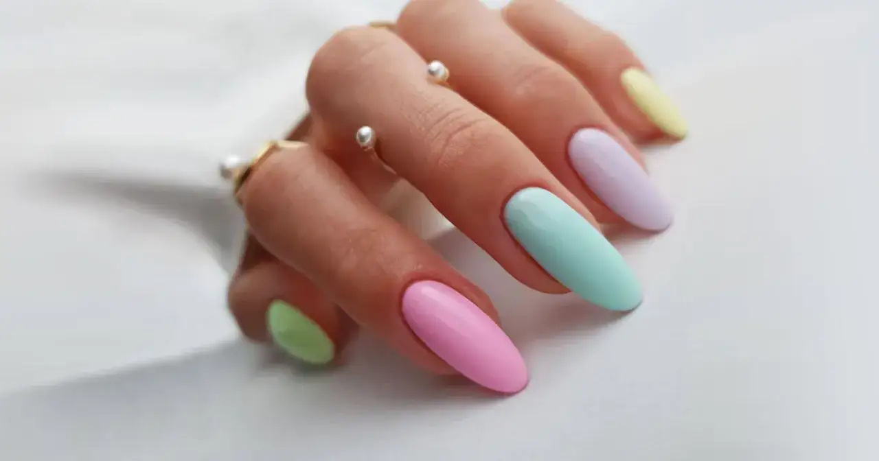 Mano con unghie lunghe e affusolate, dipinte con colori unghie primaverili pastello: rosa, verde menta, lilla e giallo. Anelli sottili con perle adornano le dita.