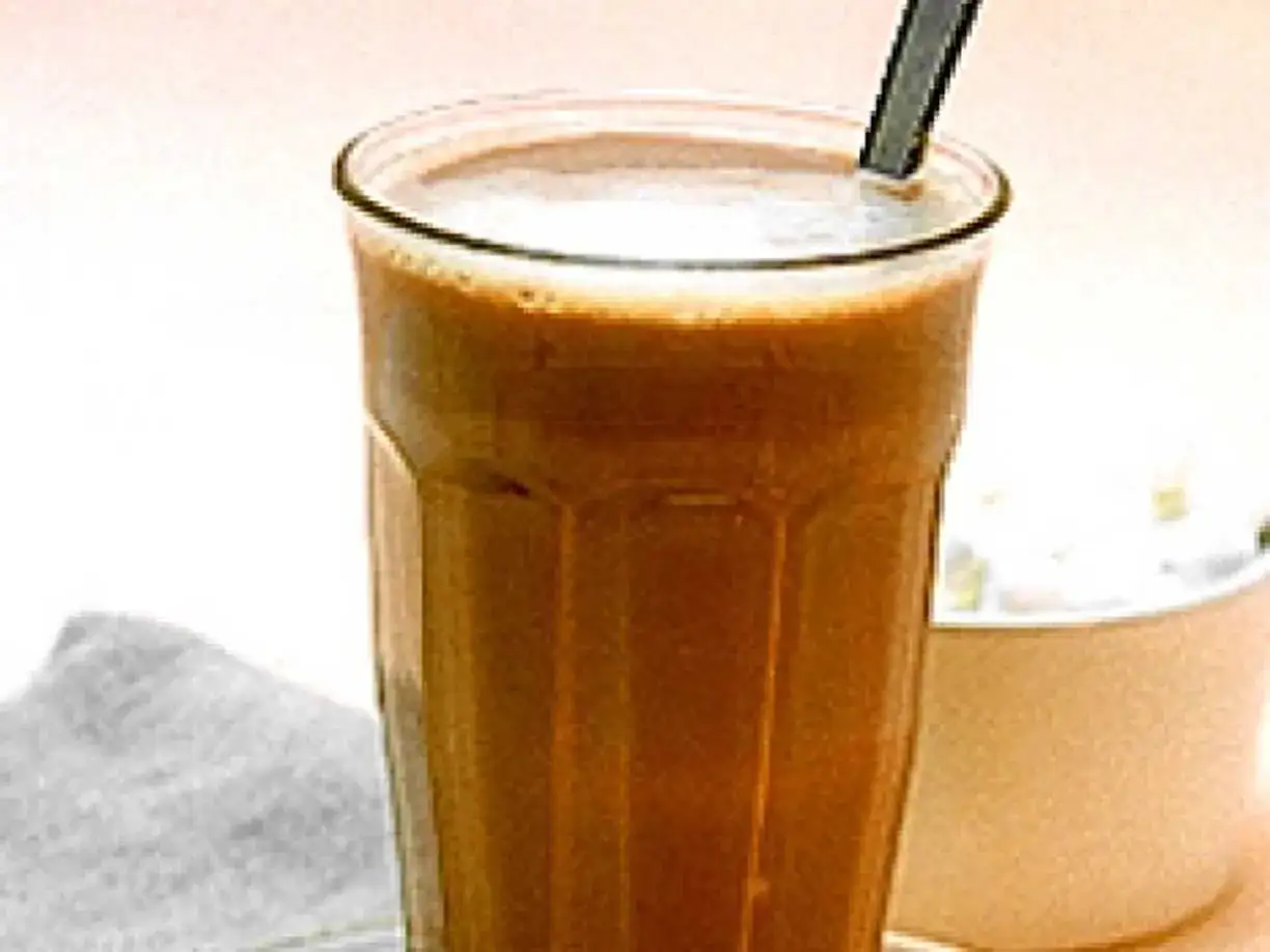 Ett glas med krämigt kaffe med choklad och en sked. Bredvid syns en skål med vispgrädde.