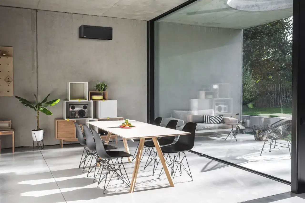 Nowoczesna klimatyzacja podstropowa w minimalistycznym salonie z jadalnią. Czarny, elegancki panel dyskretnie wtapia się w betonową ścianę.