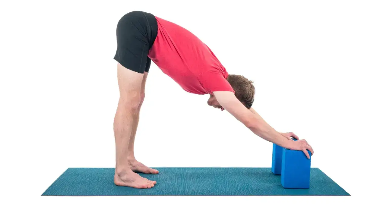 Hombre en postura de perro boca abajo, apoyando las manos en bloques de yoga para explorar variantes de uttanasana.