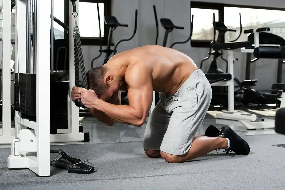 Man utför cable crunches på ett gym, böjd över repet med fokus på magmusklerna.