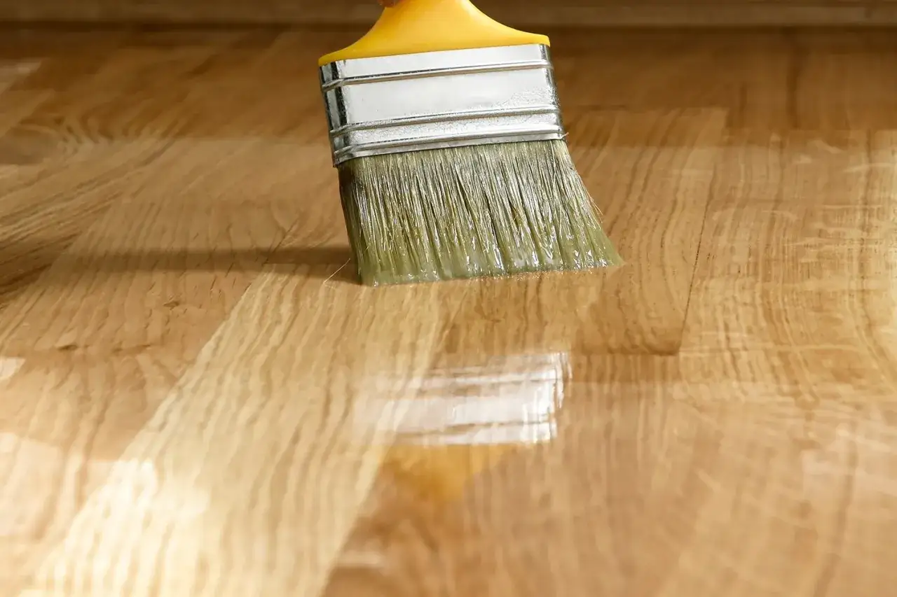 Pennello applica vernice trasparente su un piano in legno, creando una finitura mobili lucida e protettiva.