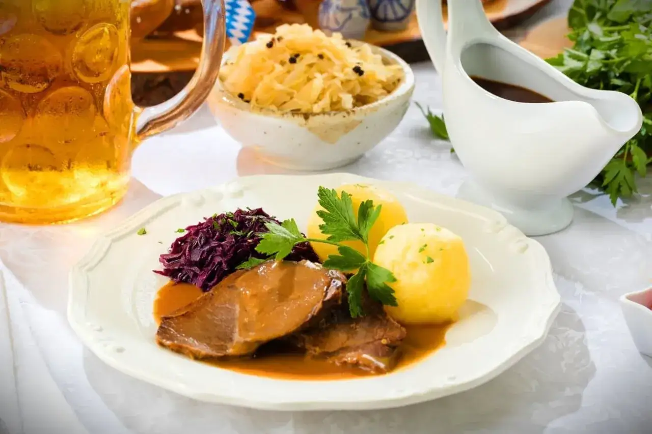 Deftiger Schweinebraten mit Kl&ouml;&szlig;en, Rotkohl und Sauerkraut. Dazu passt ein k&uuml;hles Bier.