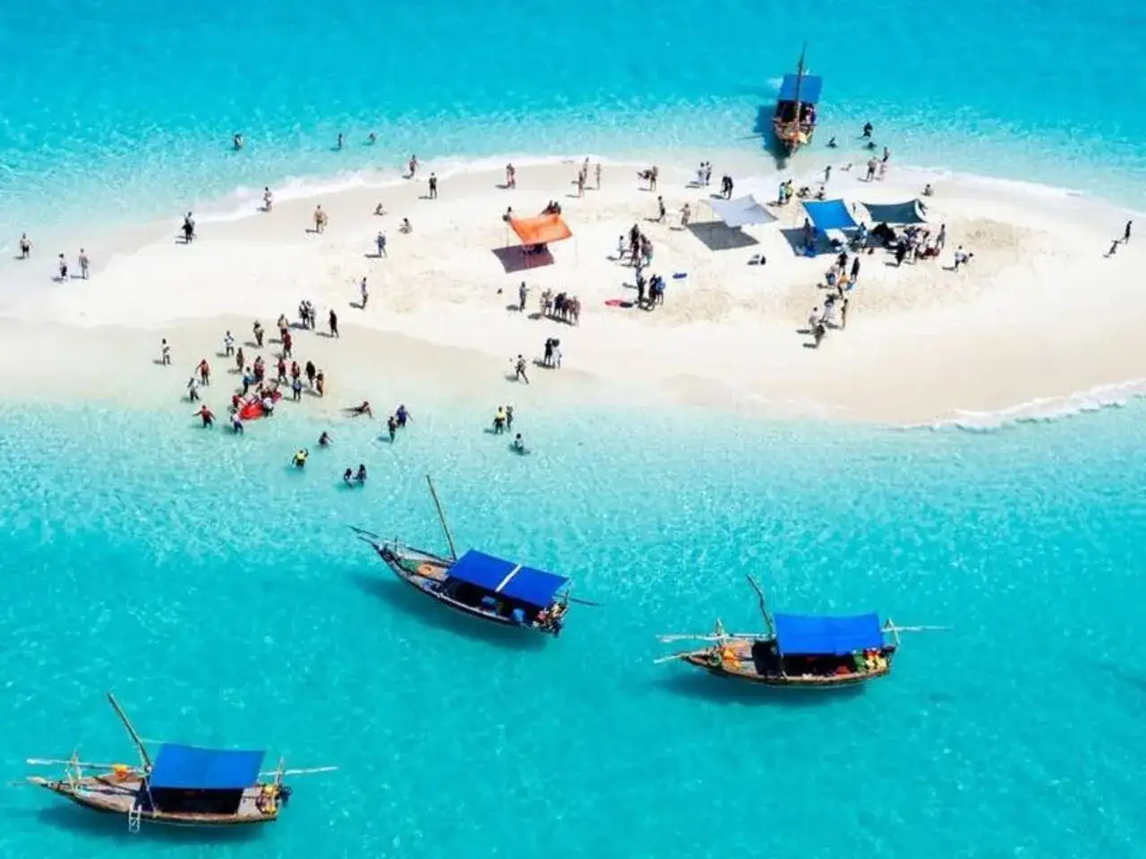 Rajski sandbank na Zanzibarze. Ludzie odpoczywają na białym piasku, a tradycyjne łodzie kołyszą się na turkusowej wodzie.