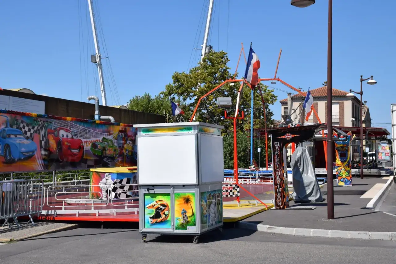 Attractions de la f&ecirc;te foraine &agrave; L'Isle-sur-la-Sorgue, avec des d&eacute;corations de voitures de course et des drapeaux fran&ccedil;ais.