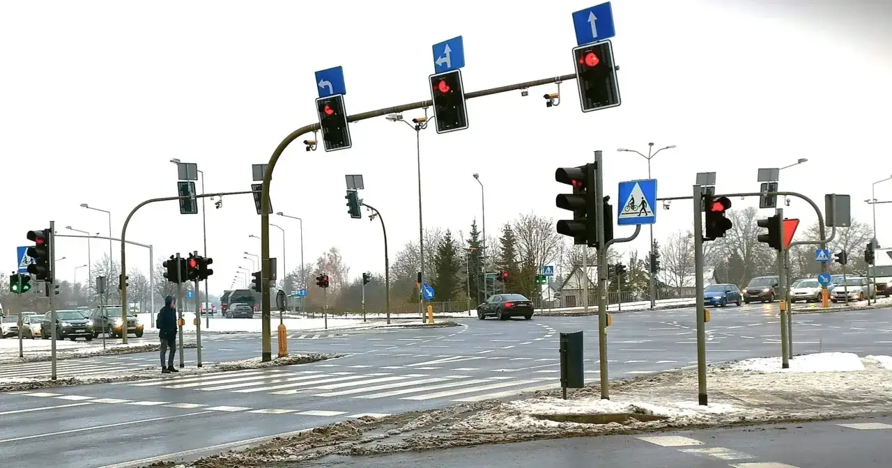 Kamery na skrzyżowaniach rejestrują ruch pojazdów i pieszych. Widać sygnalizację świetlną, znaki drogowe i przejścia dla pieszych.