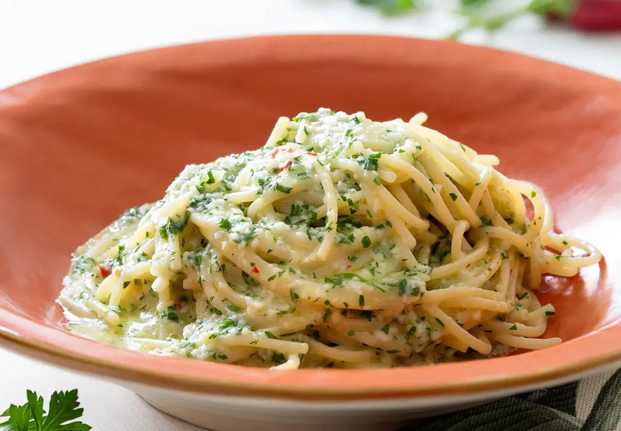 Un piatto invitante di pasta alla carrettiera, spaghetti conditi con una salsa cremosa e prezzemolo fresco, serviti in una ciotola arancione.