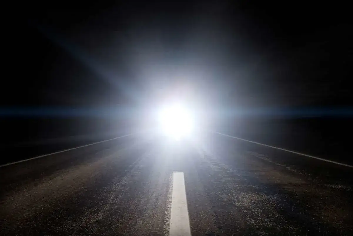 Strada buia con un abbaglio di luce accecante proveniente da un punto lontano, che illumina la corsia centrale.