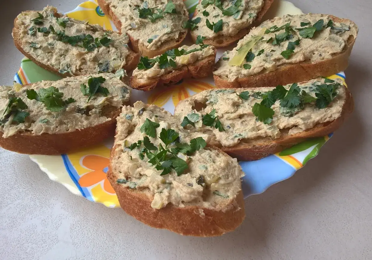 Pyszne kromki chleba z pastą z makreli i natką pietruszki, ułożone na kolorowym talerzu.