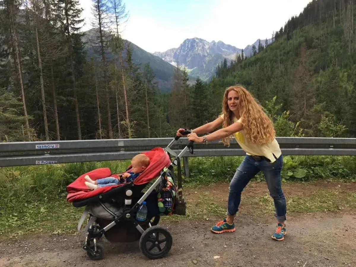 Kobieta pcha w&oacute;zek z dzieckiem po g&oacute;rskiej drodze. Idealne zakopane szlaki dla dzieci z w&oacute;zkiem, by podziwiać Tatry.