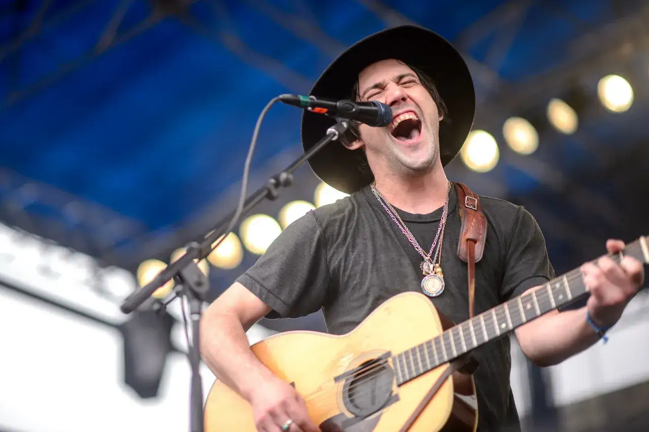 Un chanteur &agrave; la guitare, chapeau noir, yeux brillants de passion, chante &agrave; pleins poumons sous les lumi&egrave;res.