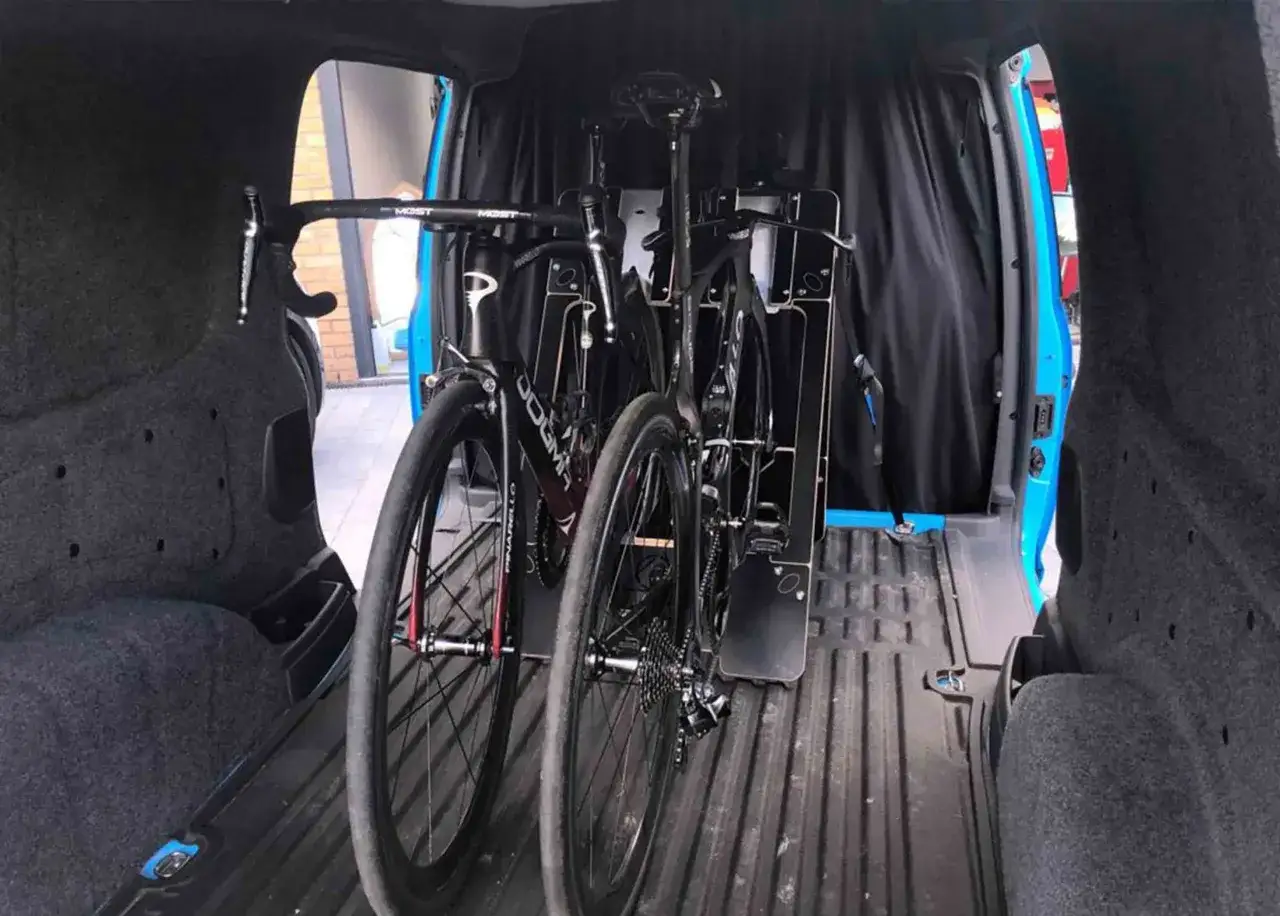 Dos bicicletas de carretera negras, listas para viajar, aseguradas dentro de una furgoneta. Así es como llevar la bici dentro de la furgoneta de forma segura.