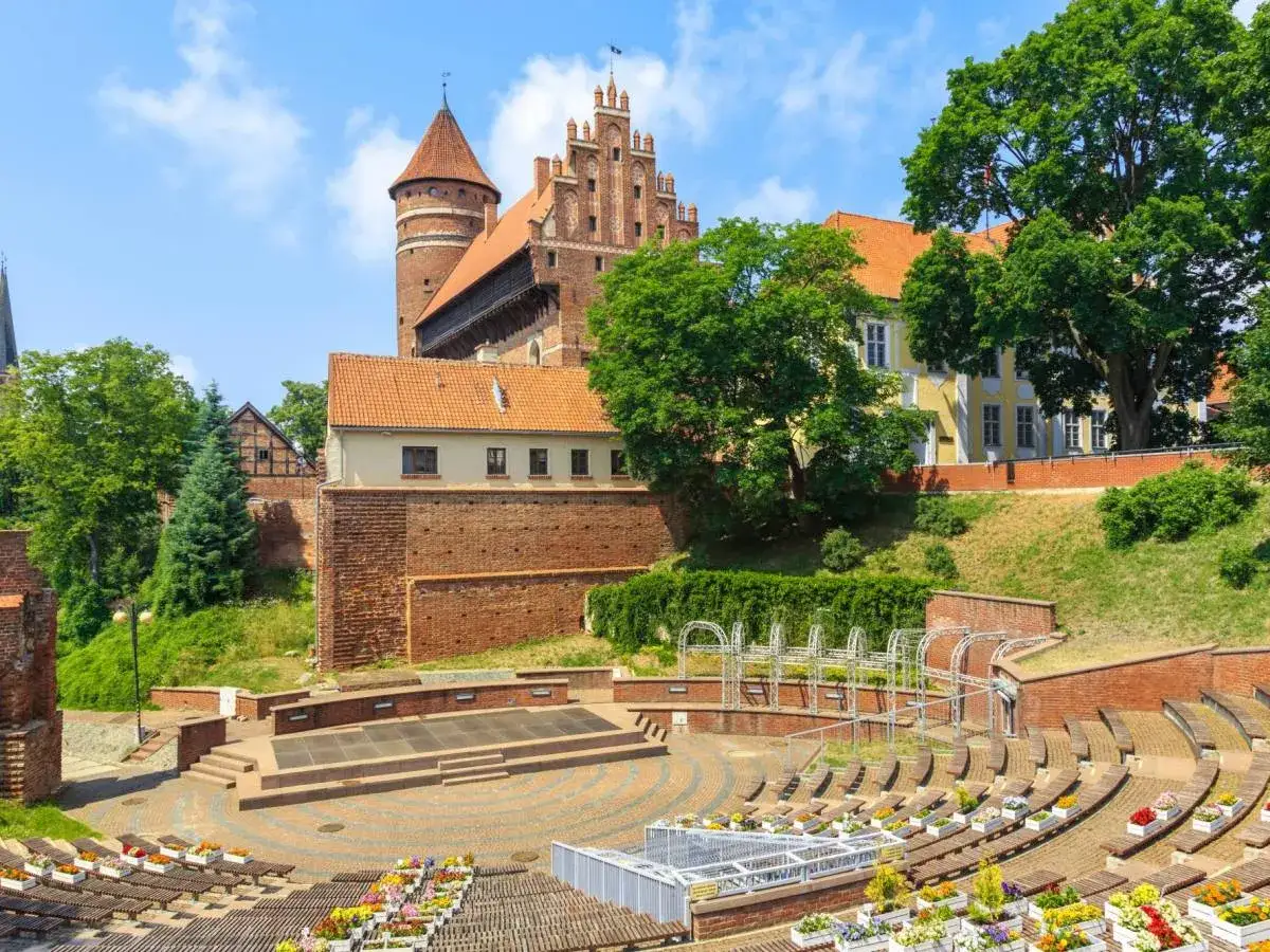 Olsztyn rynek: amfiteatr z widokiem na zamek i zabytkowe budynki, otoczony zielenią.