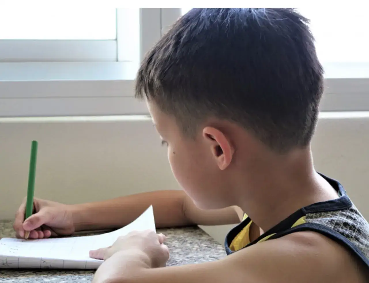 Bambino scrive un testo autobiografico per la scuola primaria, concentrato sul suo quaderno.