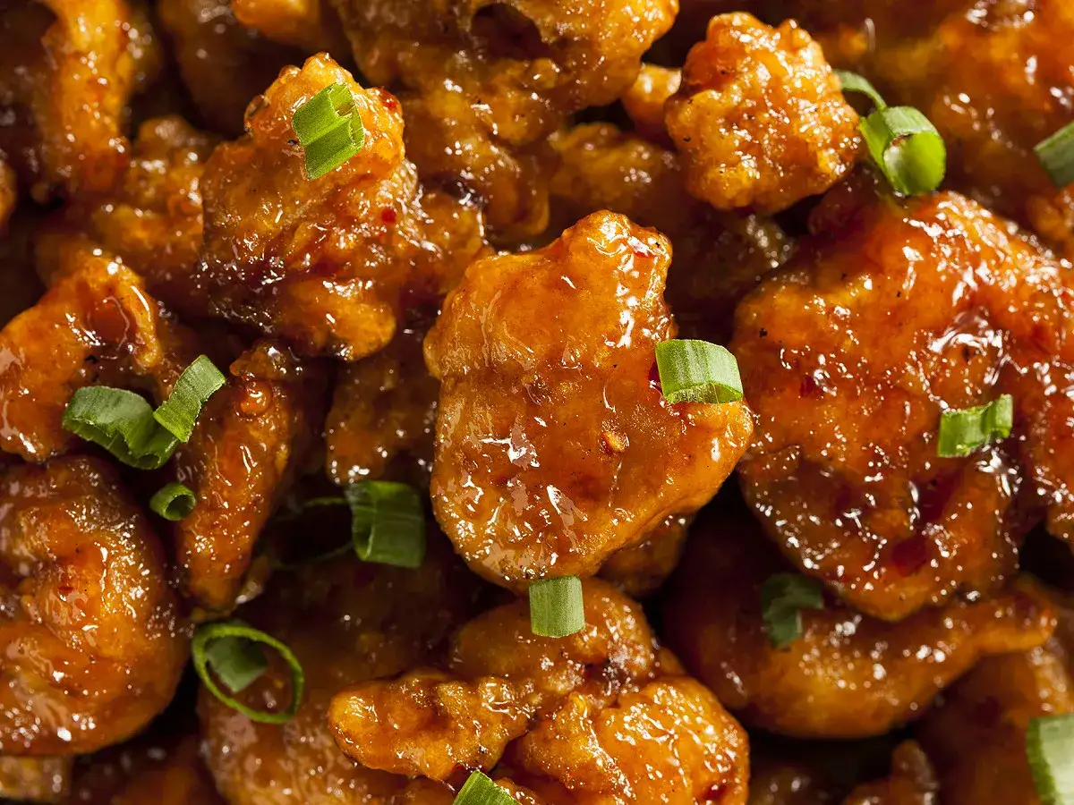 Morceaux de poulet asiatique croustillants, enrobés d'une sauce sucrée et épicée, parsemés de ciboule fraîche. Un délice de poulet asiatique marinade.