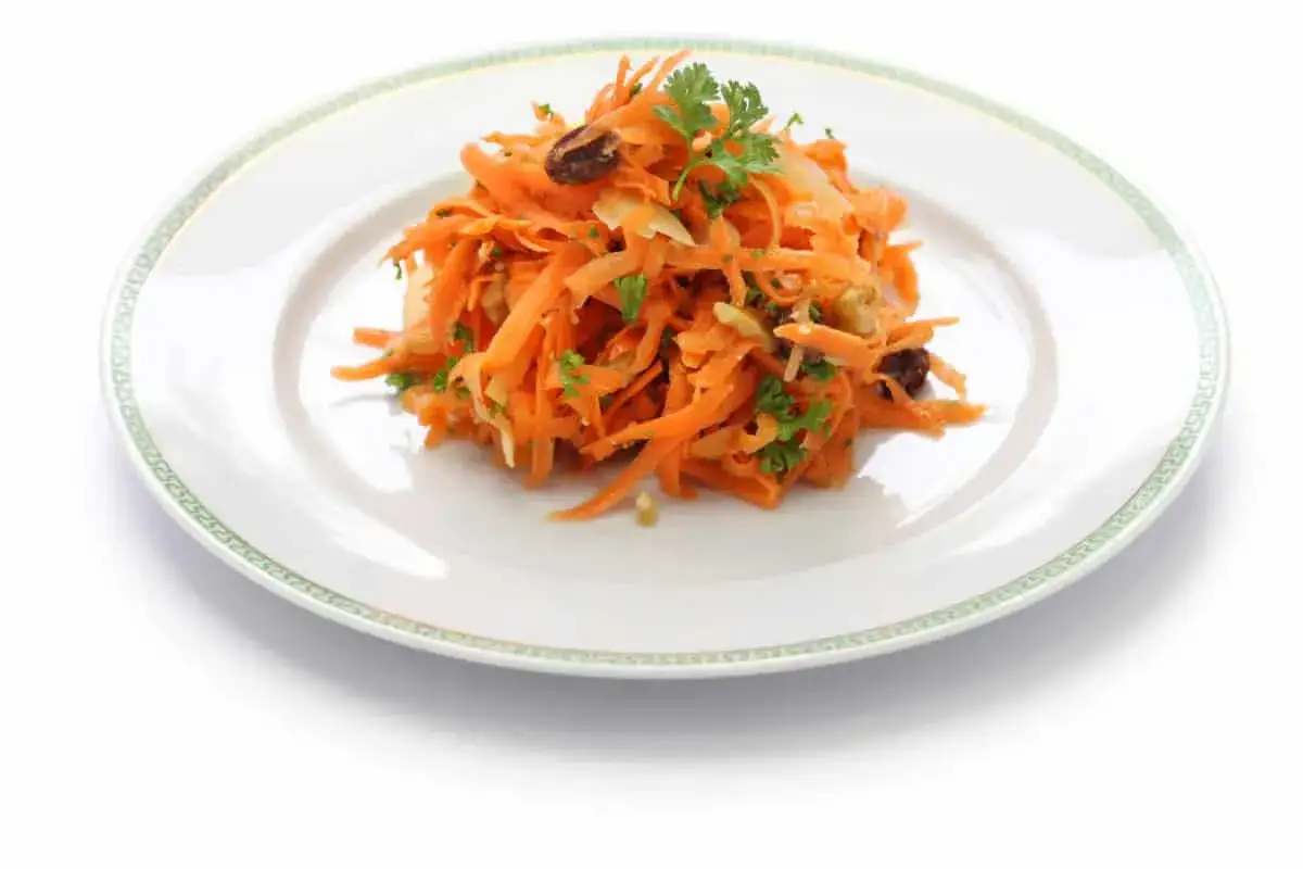 Deliciosa ensalada de zanahoria rallada con pasas y perejil fresco, servida en un plato blanco con borde verde.
