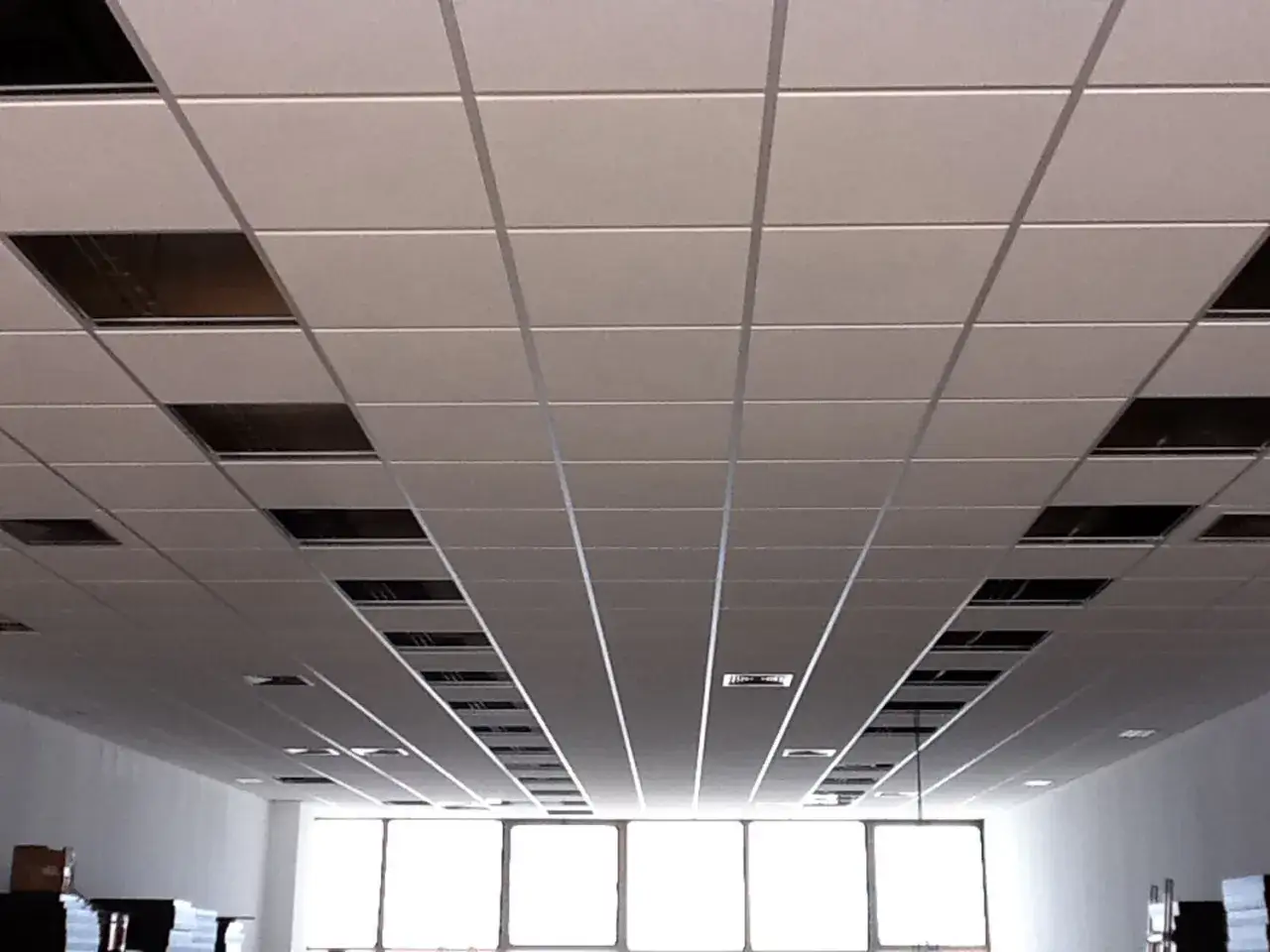 Instalaci&oacute;n de un falso techo modular con baldosas blancas y perfiles met&aacute;licos. Se aprecian huecos para luminarias o ventilaci&oacute;n.