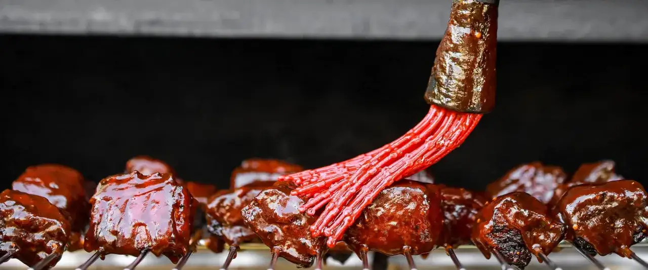 Fleischstücke werden mit einer roten Bürste mit köstlicher bbq sauce glasiert.