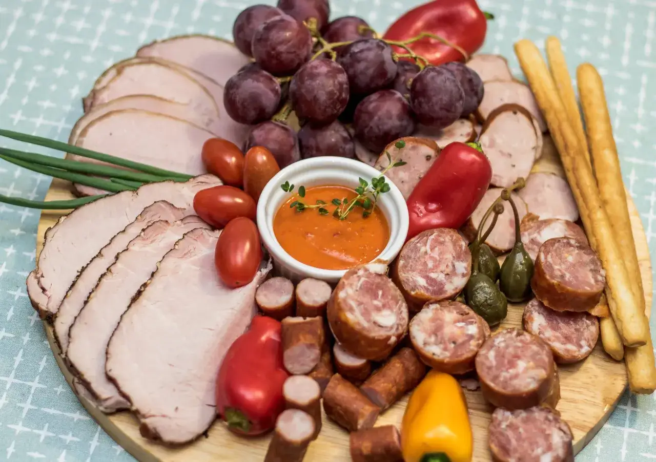 Idealna deska na sylwestra: wędliny, kiełbaski, winogrona, pomidorki, papryczki i dip.