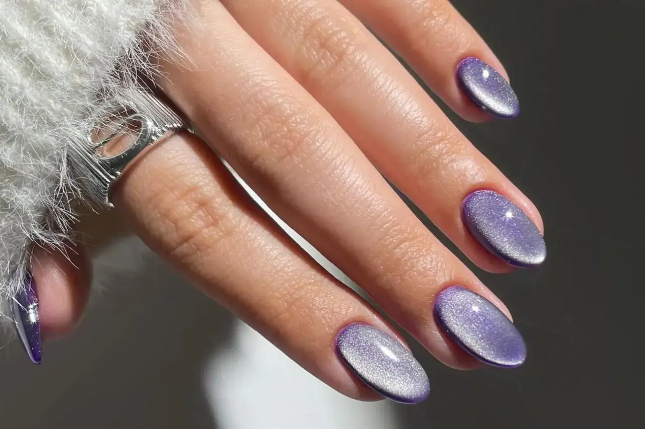 Main d'une femme avec une manucure coréenne aux ongles violets brillants, style œil de chat.
