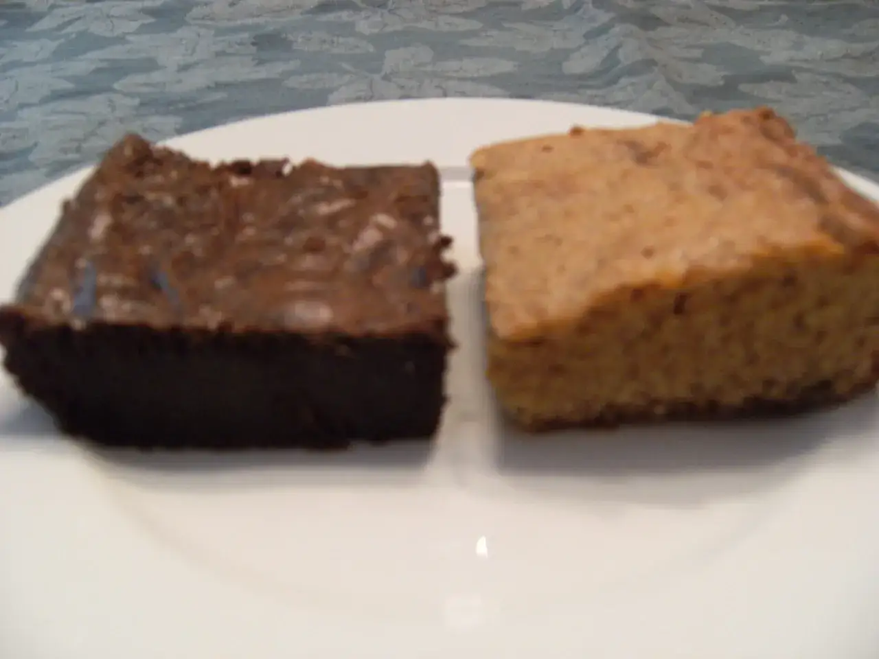 Dwa kawałki ciasta: ciemny brownie i jasny blondie, leżą obok siebie na białym talerzu.