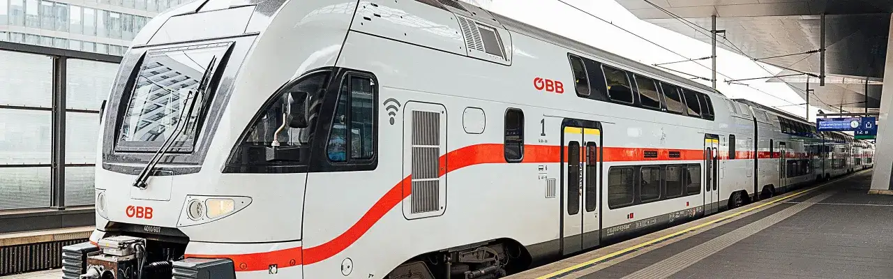 Moderner Eurocity Zug der &Ouml;BB mit roten Streifen wartet am Bahnsteig.