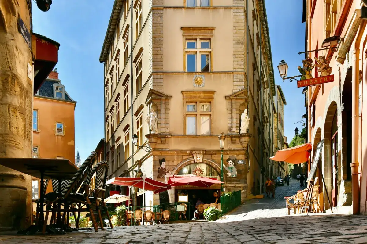 Kopfsteinpflasterstraße in Lyon, Frankreich, mit Cafétischen und einem Theater-Schild.