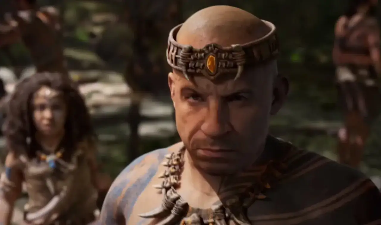 Vin Diesel w plemiennym stroju, z ozdobną opaską na głowie, zapowiada premierę ARK 2. W tle widać inne postacie.