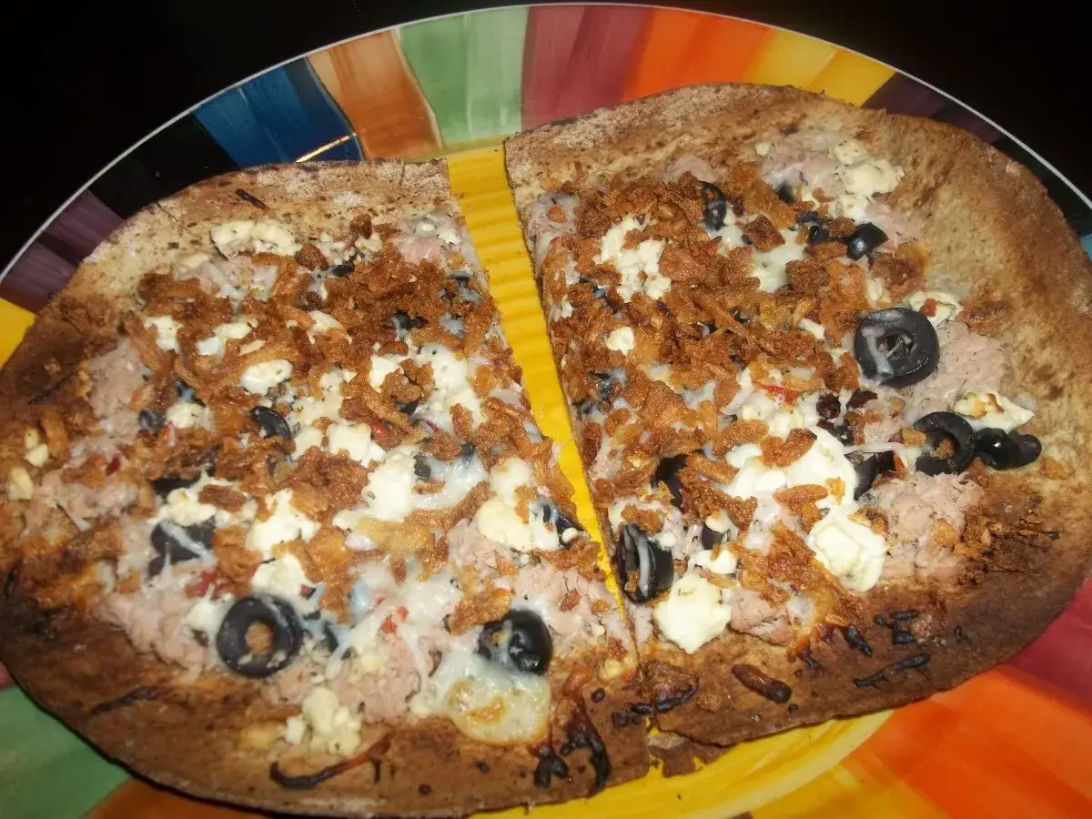 En delad pizza med tonfisk och fetaost, toppad med krispiga lökar och svarta oliver.