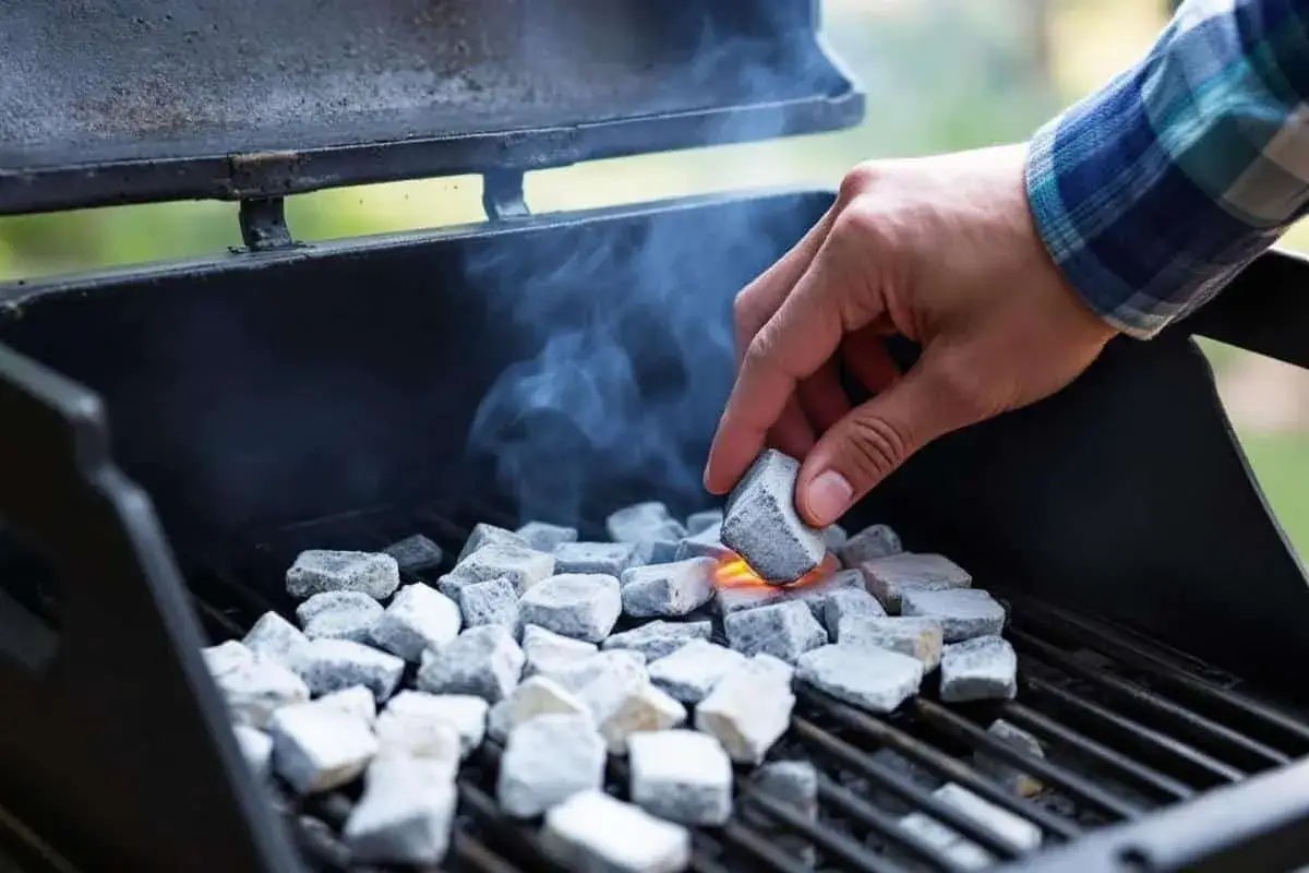 Maintenant, apprenons comment allumer un barbecue au charbon. Une main ajoute un morceau de charbon incandescent &agrave; la pile.