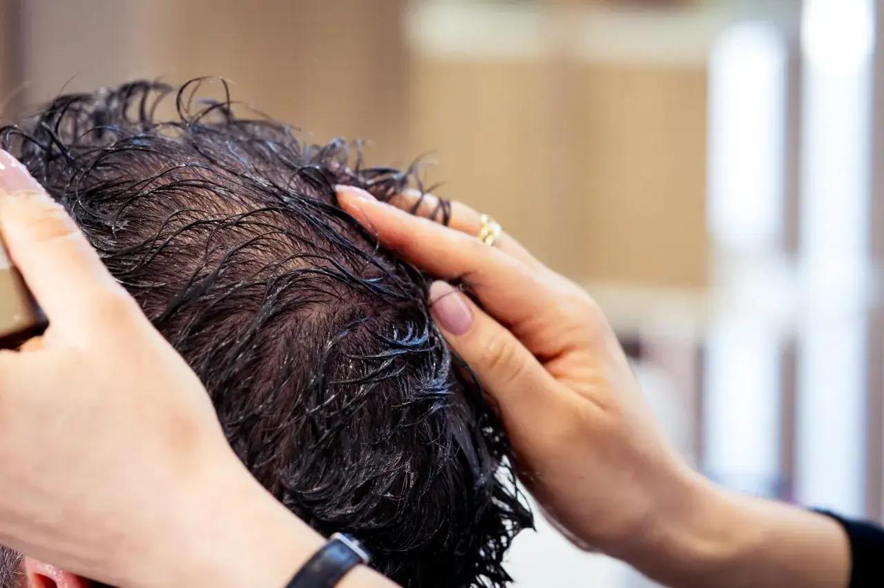 Manos aplicando producto en cabello oscuro y h&uacute;medo, mostrando la densidad capilar.