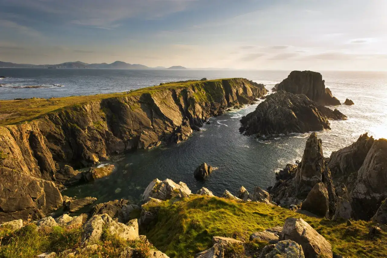 Steile Klippen und das Meer, ein Traum für jeden Irland Urlaub. Die Sonne beleuchtet die zerklüftete Küste und das türkisfarbene Wasser.