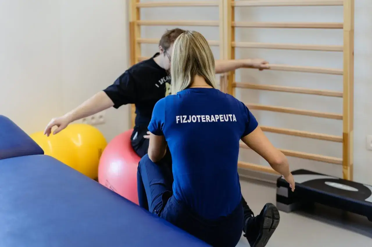 Fizjoterapeutka pomaga pacjentowi po złamaniu nasady bliższej kości łokciowej w ćwiczeniach rehabilitacyjnych na drabinkach.